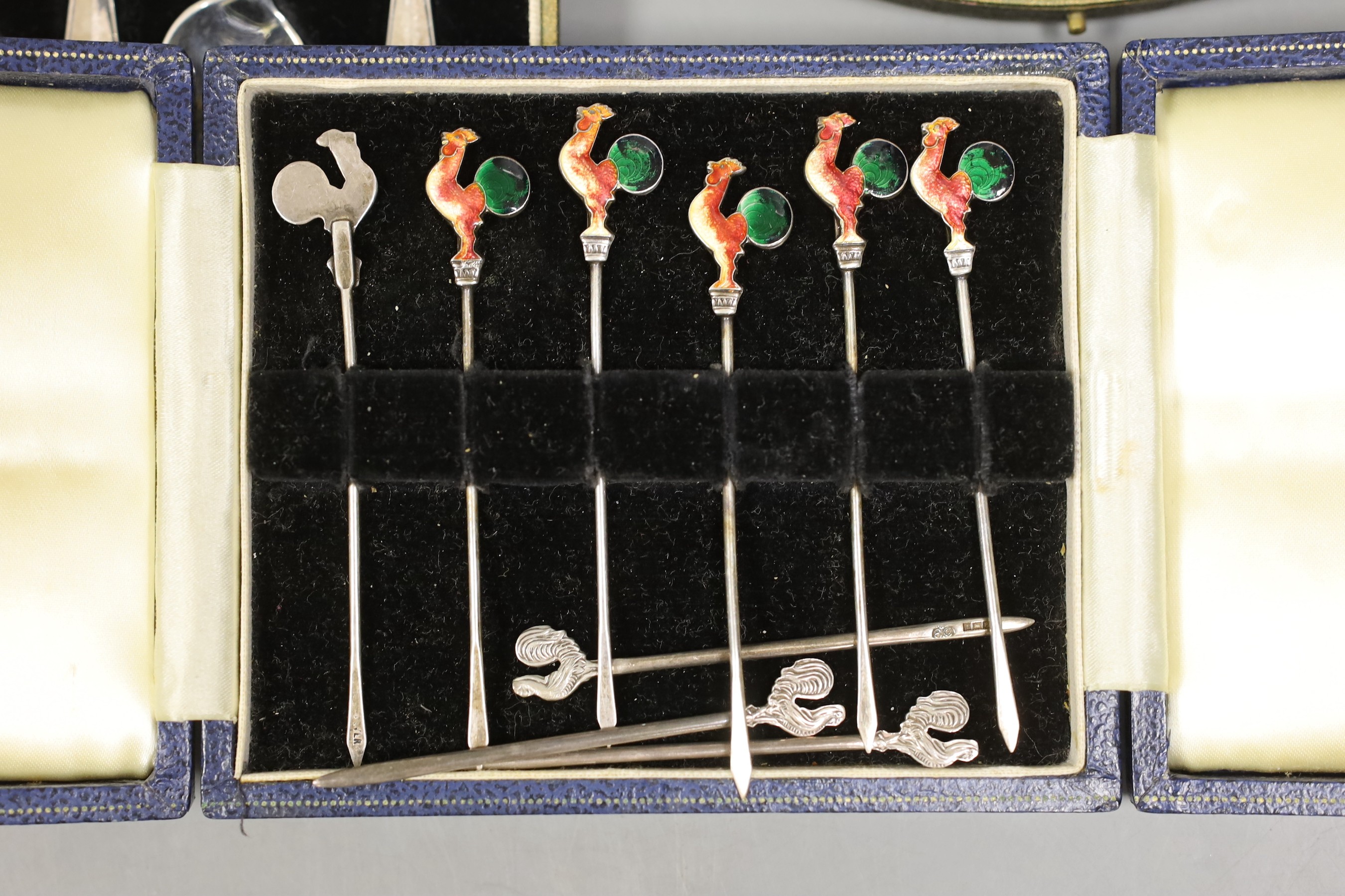 A cased set of six white metal and enamel cocktail sticks and three other cased sets including silver tea and coffee spoons and a manicure set.